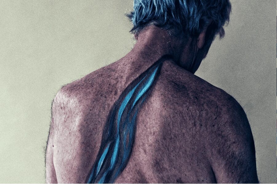 A body painting on the back of an older white man, that shows how fresh water carves out rock.