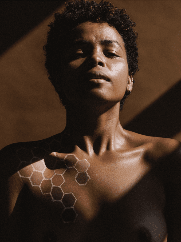 A powerful pose by Black woman with honey-comb painted on her body, showered in natural sunlight.