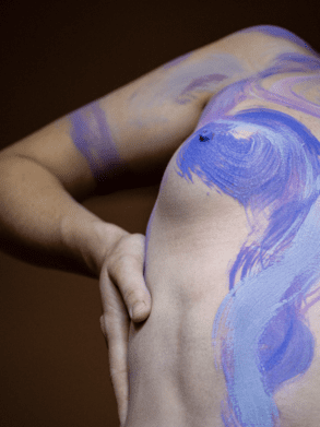 An abstract image of a naked white woman with swirls of purple body paint painted over her breast and arm