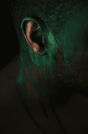 An abstract photo of a Black man's ear with dripping green paint depicting a toxic bloom.