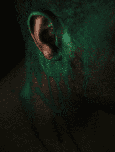 An abstract photo of a Black man's ear with dripping green paint depicting a toxic bloom.