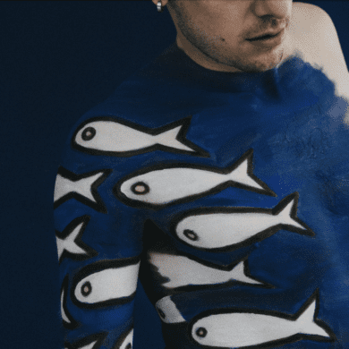 A man is painted with blue paint and white fish across his body